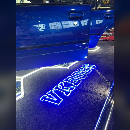 Blue LED neon VKBOSS sign displayed on the floor beside a show car